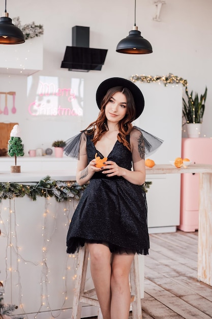 Hermosa joven con un vestido negro y un sombrero limpia una mandarina