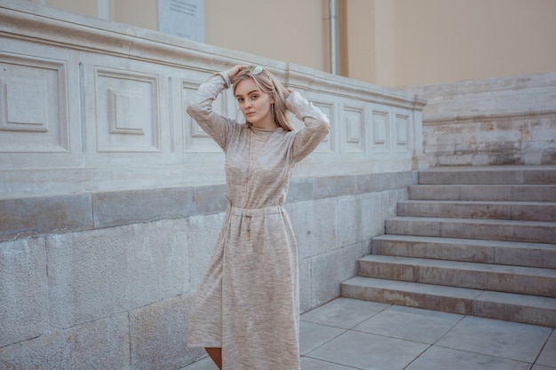 Hermosa joven con un vestido de punto beige camina por las calles de Moscú, un clima soleado de primavera