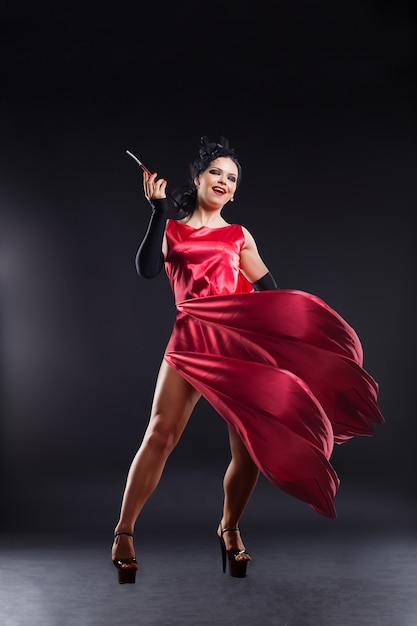 Hermosa joven con un vestido rojo con un cigarrillo, en estilo cabaret, aislado en un fondo oscuro.