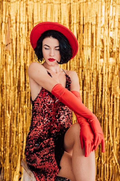 Hermosa joven en un vestido rojo y un sombrero posando sobre un fondo dorado