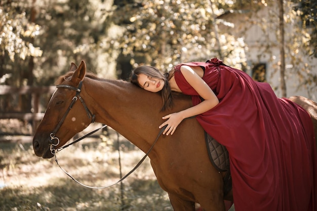 Una hermosa joven con un vestido de seda se sienta a horcajadas sobre un caballo. Paseo a caballo en un día soleado en el bosque.