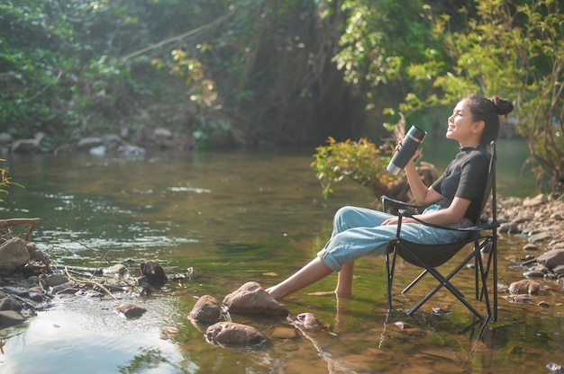 Una hermosa joven viajera está disfrutando de la naturaleza tomando café por la mañana sobre el lago, la relajación, las vacaciones de campamento y el concepto de viaje