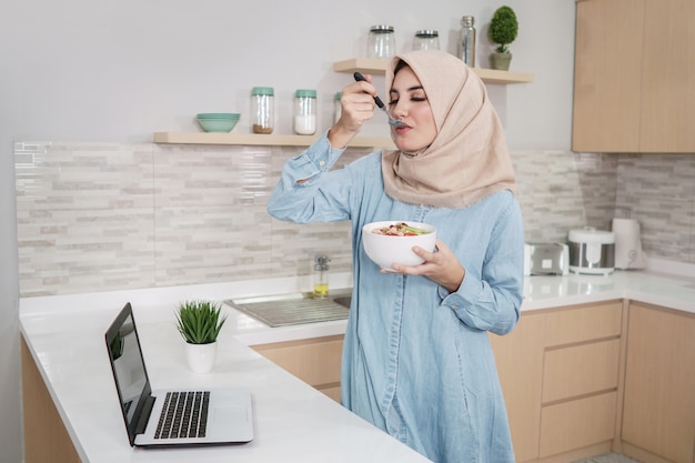 Hermosa joven vistiendo hijab comiendo un tazón de ingenio granola