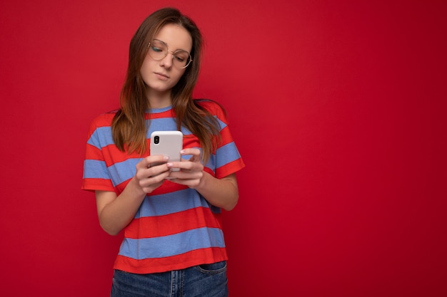Foto hermosa joven vistiendo ropa casual que se encuentran aisladas sobre antecedentes navegando en internet a través del teléfono mirando la pantalla del móvil