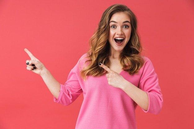 Hermosa joven vistiendo ropa casual que se encuentran aisladas sobre pared rosa, presentando espacio de copia