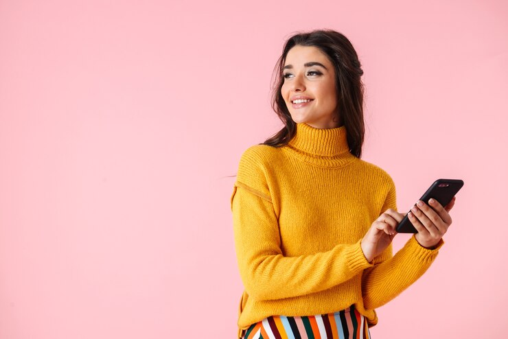 Foto hermosa joven vistiendo ropas coloridas que se encuentran aisladas sobre rosa, mediante teléfono móvil