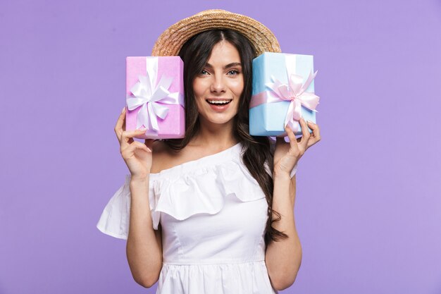 Hermosa joven vistiendo traje de verano que se encuentran aisladas sobre la pared violeta, mostrando dos cajas de regalo