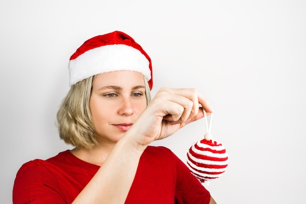 Hermosa jovencita con accesorios de Santa Claus como gorro de Papá Noel y traje rojo aislado sobre fondo blanco. Foto de Navidad. Brasileña, caucásica, cabello rubio, ojos verdes.