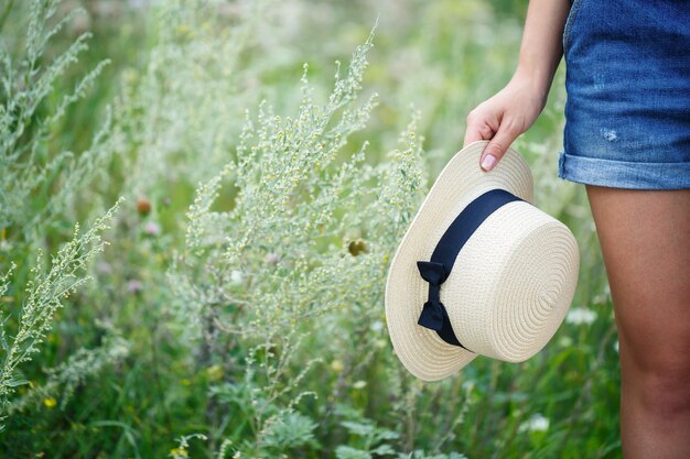 Hermosa jovencita en overoles de mezclilla y un sombrero ligero caminando en el parque