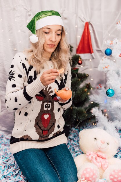 Hermosa jovencita pela mandarinas cerca del árbol de navidad