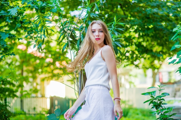 Hermosa jovencita posando al aire libre, con un vestido blanco de moda. Estilo de verano.