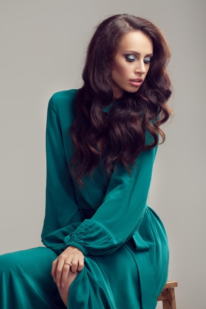 Hermosa jovencita posando en el estudio. pelo negro largo y rizado. vestido azul verdoso.