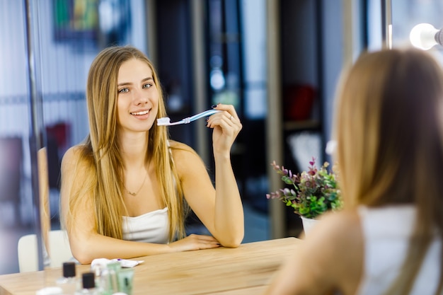 Hermosa jovencita a punto de cepillarse los dientes frente a un espejo