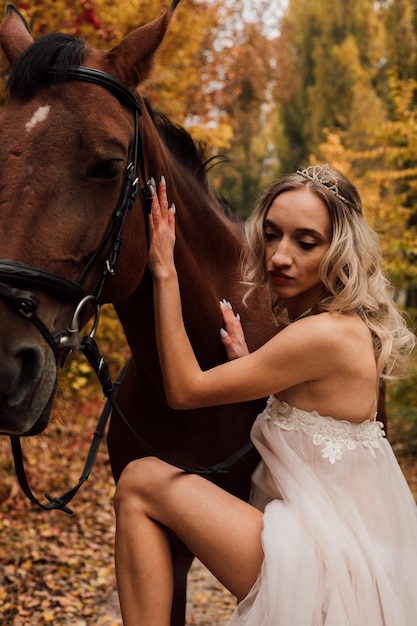 Hermosa jovencita rubia posando en un parque de otoño con un caballo