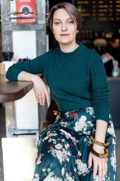 Hermosa linda chica en el café mirando a la cámara con café sonriendo. Jersey de punto verde. chica vestida a la moda. chica mira el teléfono. dama de negocios