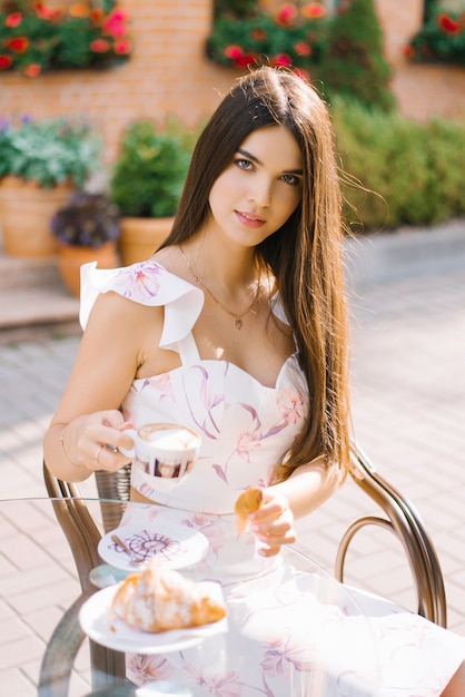 Hermosa linda chica sentada en una mesa en un café de la calle y tomando café. desayuno o almuerzo de una mujer bonita.