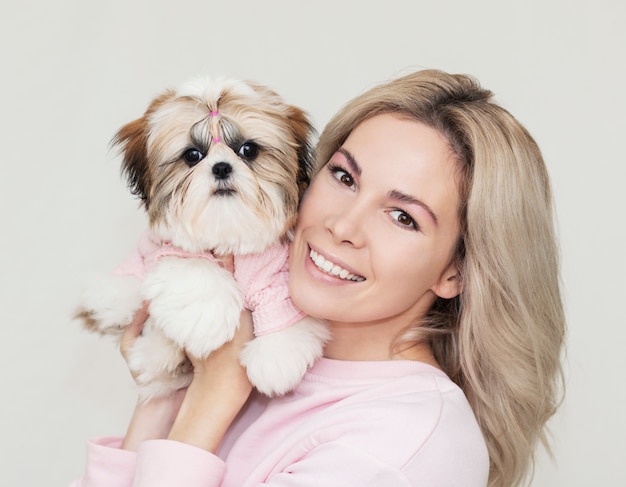 Hermosa linda chica sosteniendo un cachorro shih tzu bien arreglado en un suéter rosa