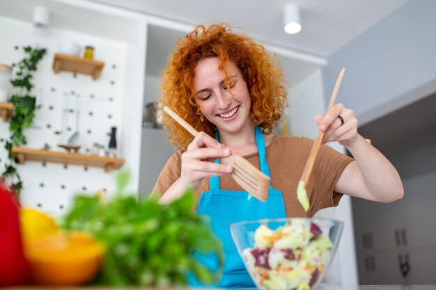 Foto hermosa linda joven sonriente en la cocina está preparando una ensalada vegana en ropa casual