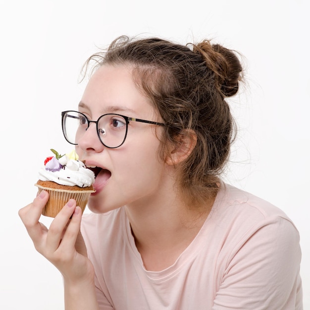 Hermosa linda jovencita con gafas comiendo pastel de crema sobre fondo blanco.