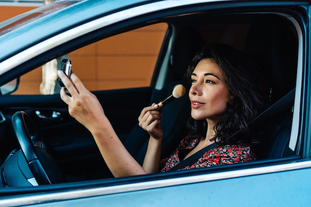 Hermosa linda mujer sonriente en coche usando maquillaje mientras espera luz roja