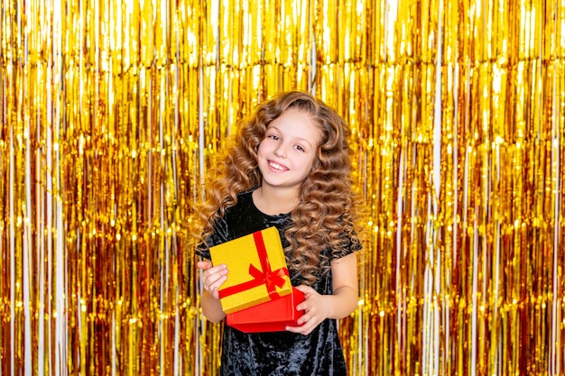 Hermosa linda niña alegre sobre un fondo dorado de vacaciones con una caja de regalo en sus manos