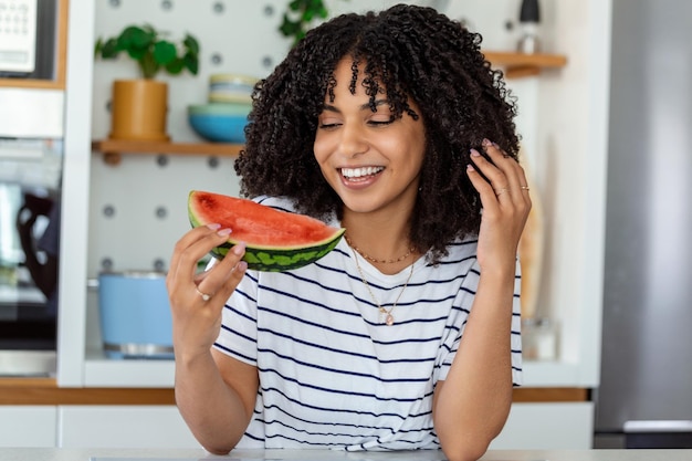 Hermosa madre africana comiendo sandía en la cocina de casa