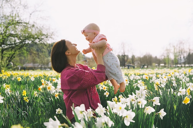 Hermosa madre amorosa y niña en el campo de flores de narcisos en primavera Mujer joven con su linda hijita jugando al aire libre Familia en la naturaleza en Arboretum Eslovenia