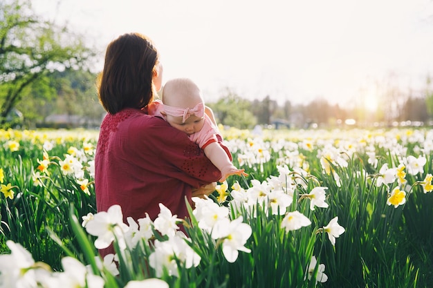 Hermosa madre amorosa y niña en el campo de flores de narcisos en primavera Mujer joven con su linda hijita jugando al aire libre Familia en la naturaleza en Arboretum Eslovenia