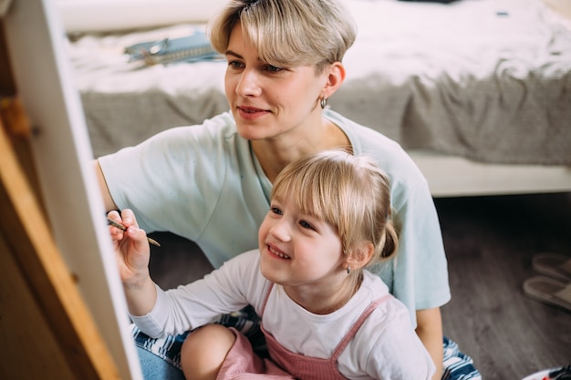 Hermosa madre artista y su hijo pintan un cuadro en casa con pinturas acrílicas