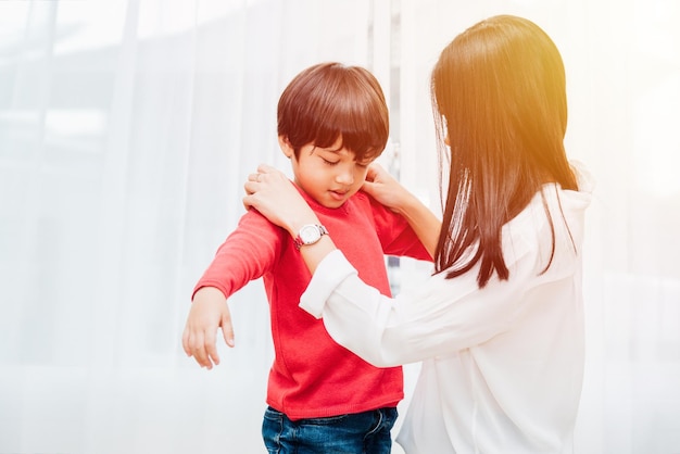 Hermosa madre asiática feliz ayudando a vestirse a su hijo en casa para estar listo antes de ir a la escuela, concepto de regreso a la escuela
