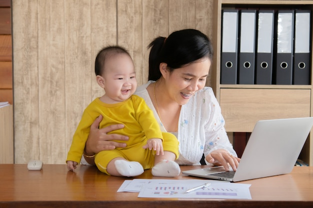 Hermosa madre asiática pasó tiempo con un niño pequeño bebé hablando, jugando en el lugar de trabajo, adorable hijo travieso feliz riendo en la computadora portátil mamá agarrada en la mano, madre soltera alimentando tareas múltiples trabajando en casa