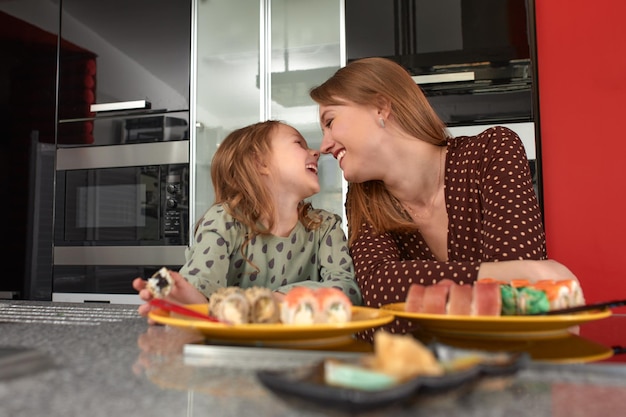 Hermosa madre caucásica e hija comiendo rollos y sushi en el almuerzo familiar en casa Comida de entrega Comida tradicional japonesa