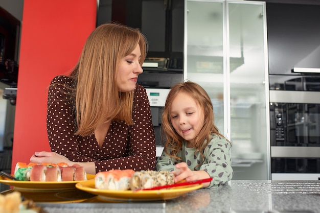 Hermosa madre caucásica e hija comiendo rollos y sushi en el almuerzo familiar en casa Comida de entrega Comida tradicional japonesa