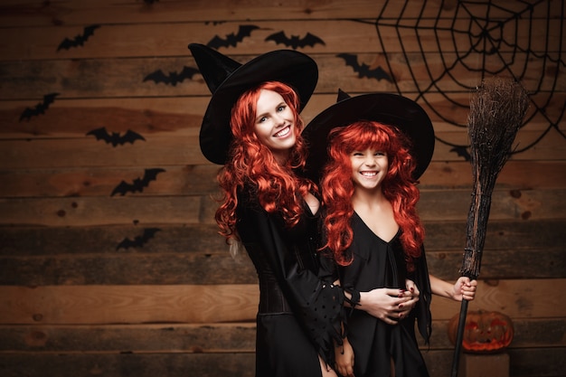 Hermosa madre caucásica y su hija con el pelo rojo largo en trajes de bruja que celebran la presentación de Halloween