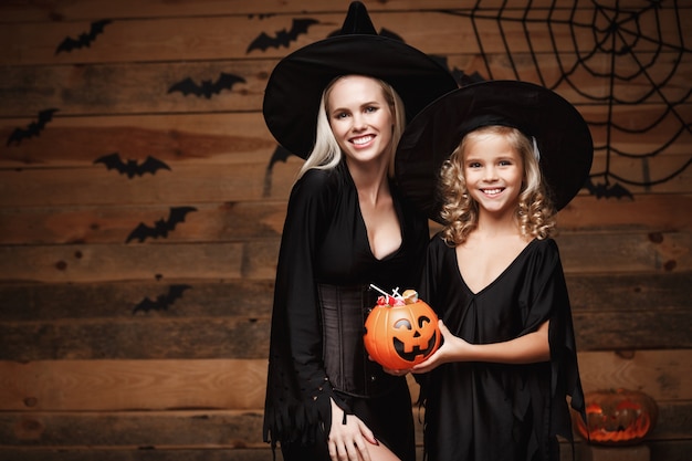 hermosa madre caucásica y su hija en trajes de bruja que celebran Halloween con el intercambio de dulces de Halloween