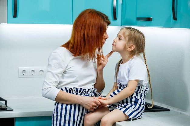 Hermosa madre e hija se abrazan y sonríen con alegría, sentadas en la cocina. Concepto de familia, niños, maternidad y cocina. Relaciones familiares felices