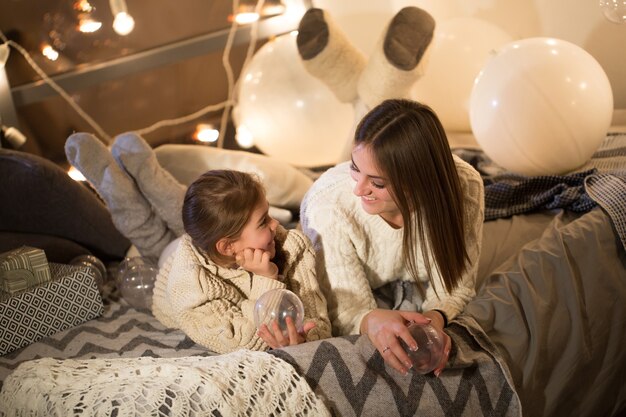 Hermosa madre e hija acostada en la cama en la víspera de Navidad en el acogedor interior de la casa. Año nuevo.