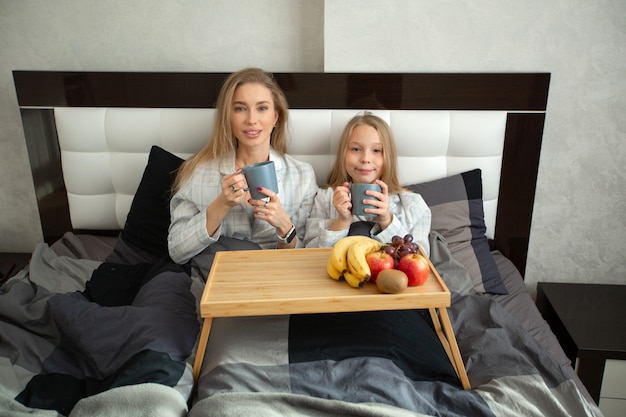 Hermosa madre e hija comiendo en la cama