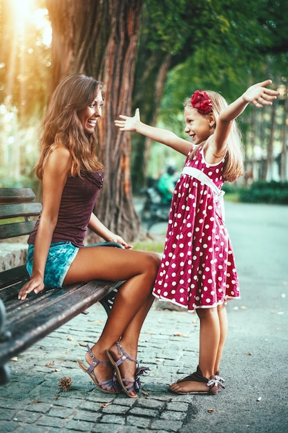 Hermosa madre e hija se divierten en el parque en primavera. La niña levanta las manos para abrazar a su madre.