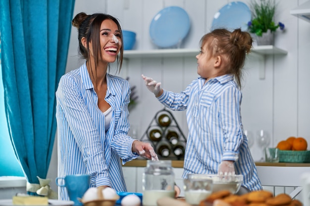 Hermosa madre e hija juegan en la cocina con harina. La niña se untó la nariz y se rió.