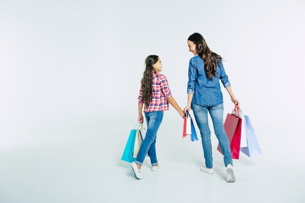 Hermosa madre e hija linda en ropa casual con bolsas de compras en las manos hacen compras en el centro comercial aislado en blanco