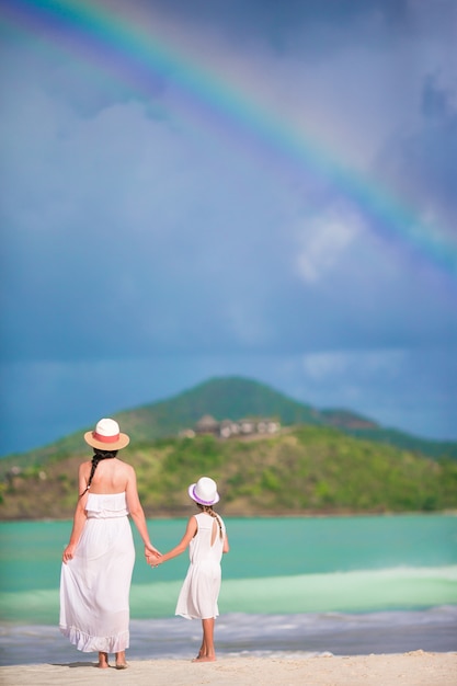 Hermosa madre e hija en la playa caribeña con increíble arco iris