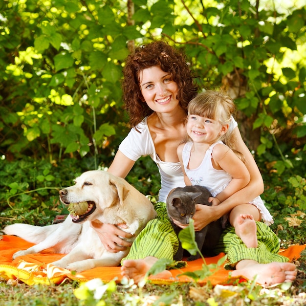 Hermosa madre e hija relajándose en la naturaleza con mascotas