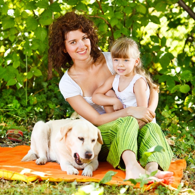 Hermosa madre e hija relajándose en la naturaleza con su perro