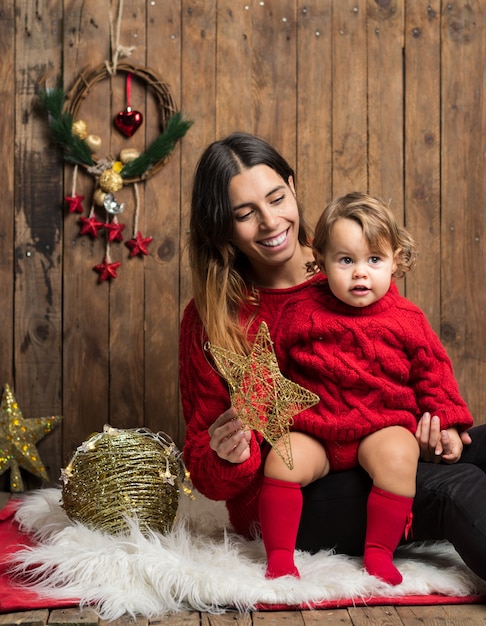 Hermosa madre e hija vestidas igual con suéteres rojos sobre fondo de madera de Navidad