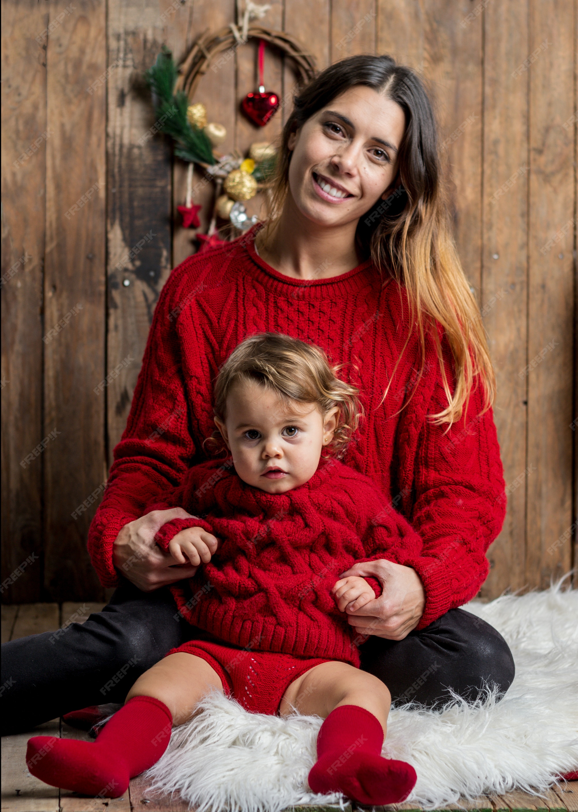 Hermosa madre e hija vestidas igual con suéteres rojos fondo de madera de navidad | Foto