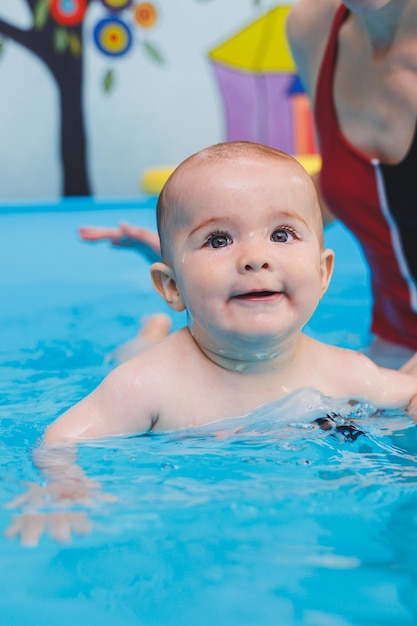 Una hermosa madre enseña a su pequeño hijo a nadar en la piscina Un niño se divierte en el agua con su madre Desarrollo infantil Primeras lecciones de natación para niños