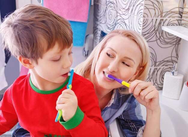 Hermosa madre feliz y pequeño hijo en bathrom cepillarse los dientes juntos