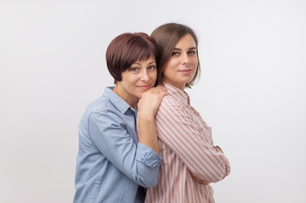 Hermosa madre madura y su hija adulta se abrazan mirando a la cámara y sonriendo