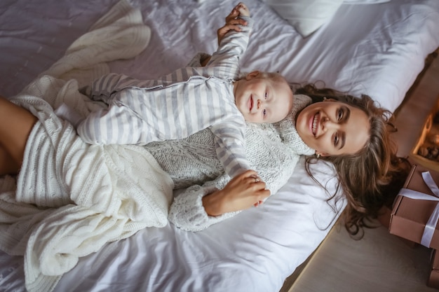 Hermosa madre con ojos azules y el bebé acostado en el dormitorio en la cama en la vista superior de la sábana blanca